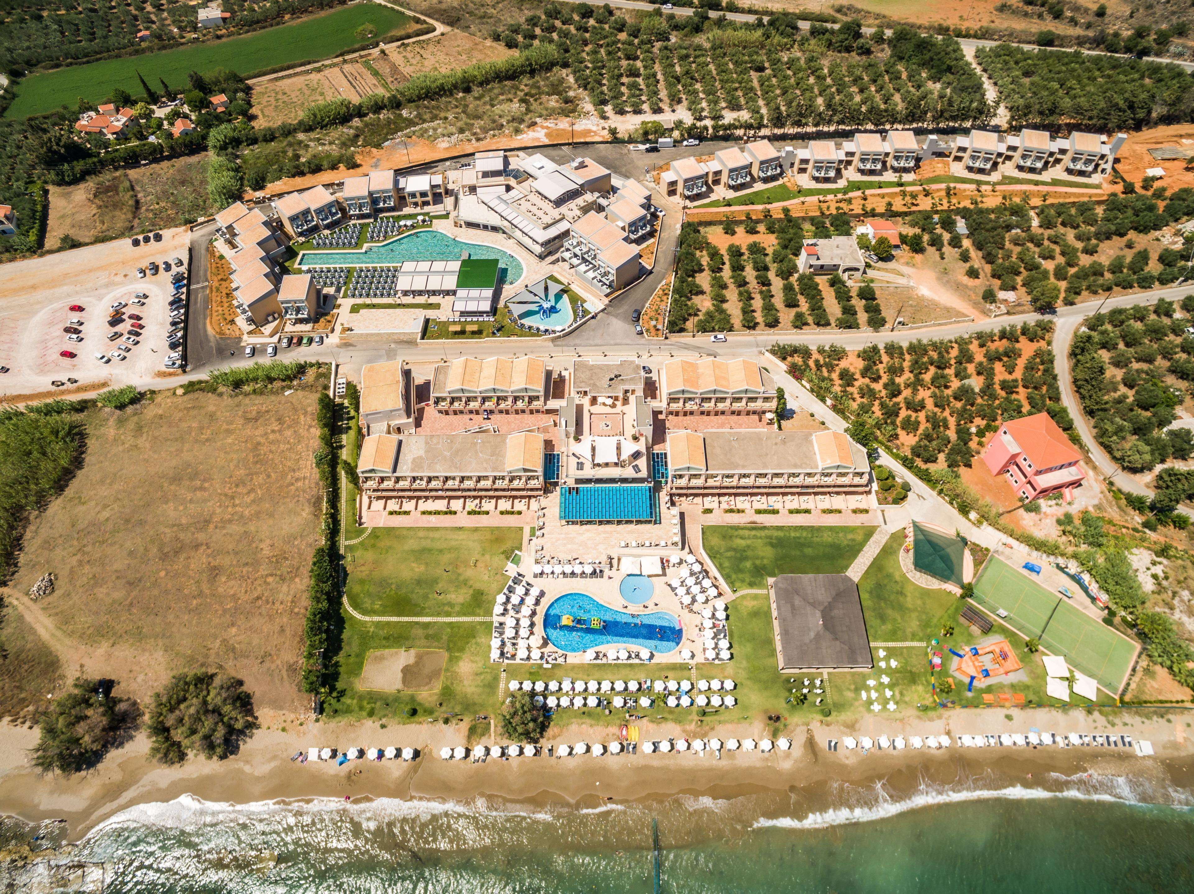 Vista aérea de un complejo turístico con varias edificaciones, una piscina y una zona de playa.