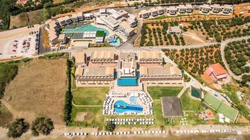 Vista aérea de un complejo turístico con varias edificaciones, una piscina y una zona de playa.