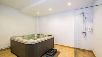 Un baño moderno con ducha envuelta en vidrio, jacuzzi integrado y un escalón para facilitar el acceso.