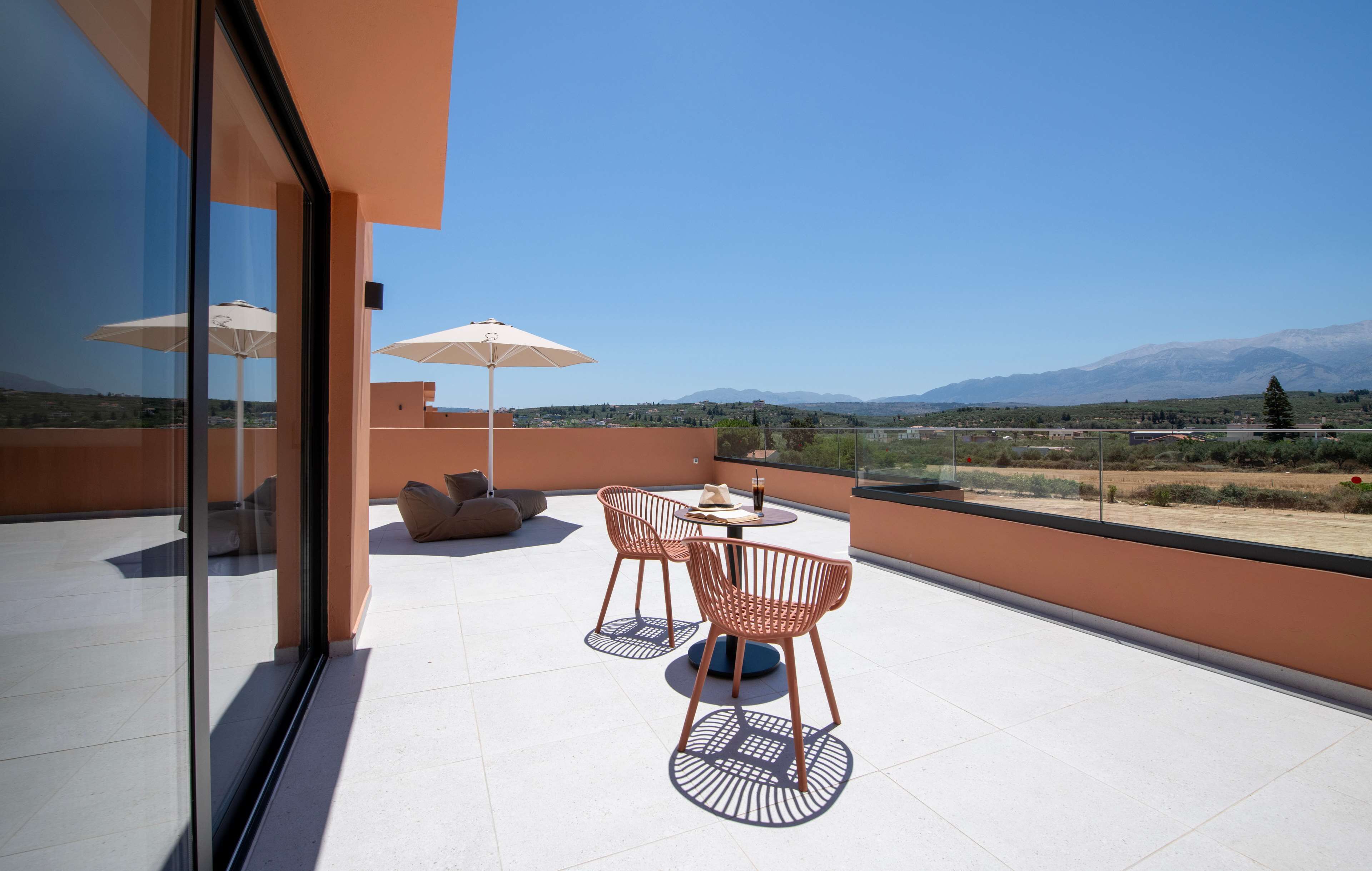 Une terrasse extérieure moderne, dotée d’une balustrade en verre, de deux tables rondes avec des chaises et de parasols.