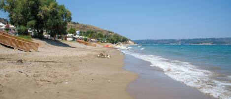 A sandy beach with a wooden walkway, a boat, and a clear blue sky.