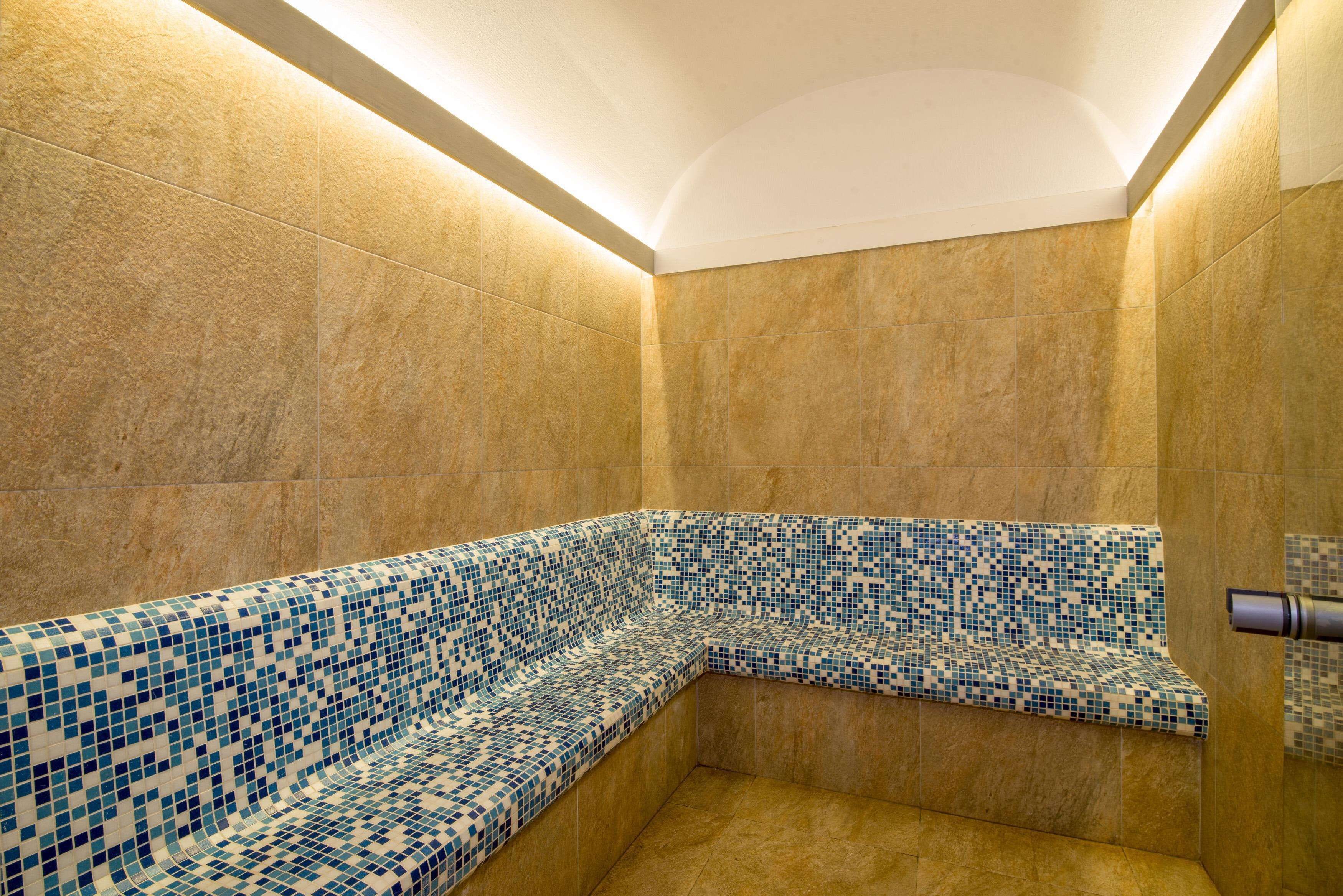 Une douche d’angle avec des bancs recouverts de mosaïques et un luminaire au plafond.