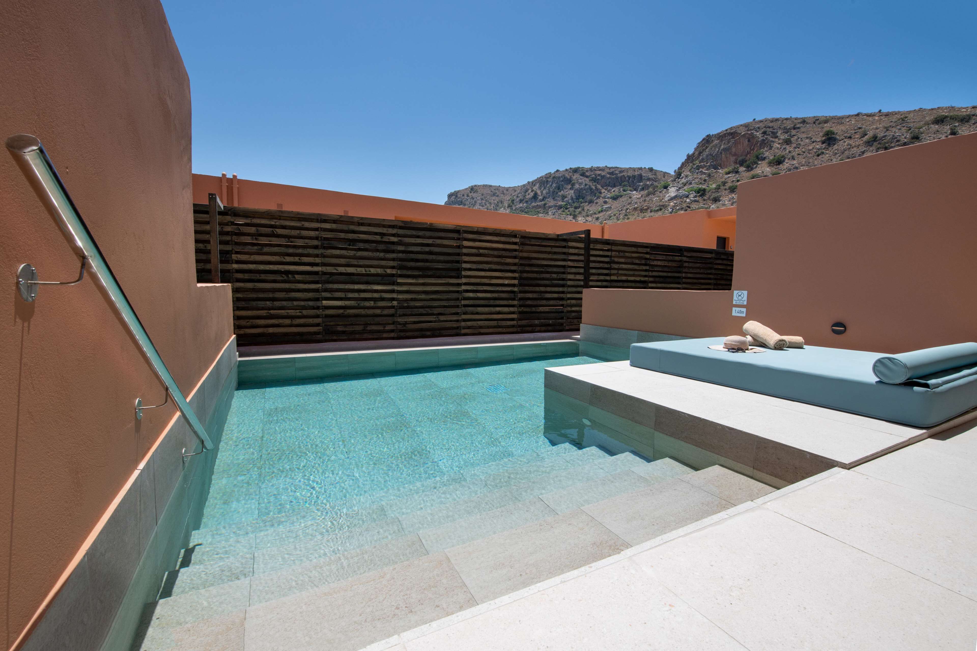 Ein Poolbereich mit Holzzaun, eine kleine Sitzecke mit Handtuch und Blick auf eine gebirgige Landschaft.