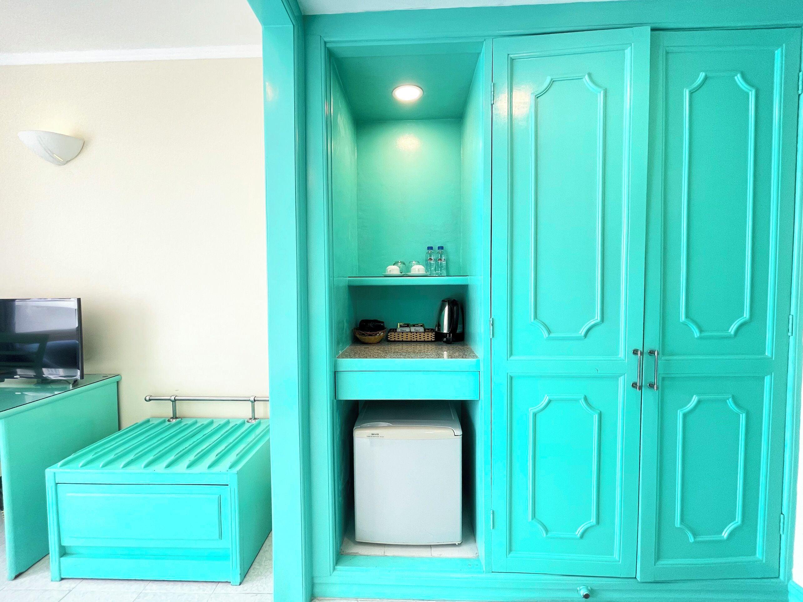 A teal-colored room with a television, a small refrigerator, and a cabinet with shelves.