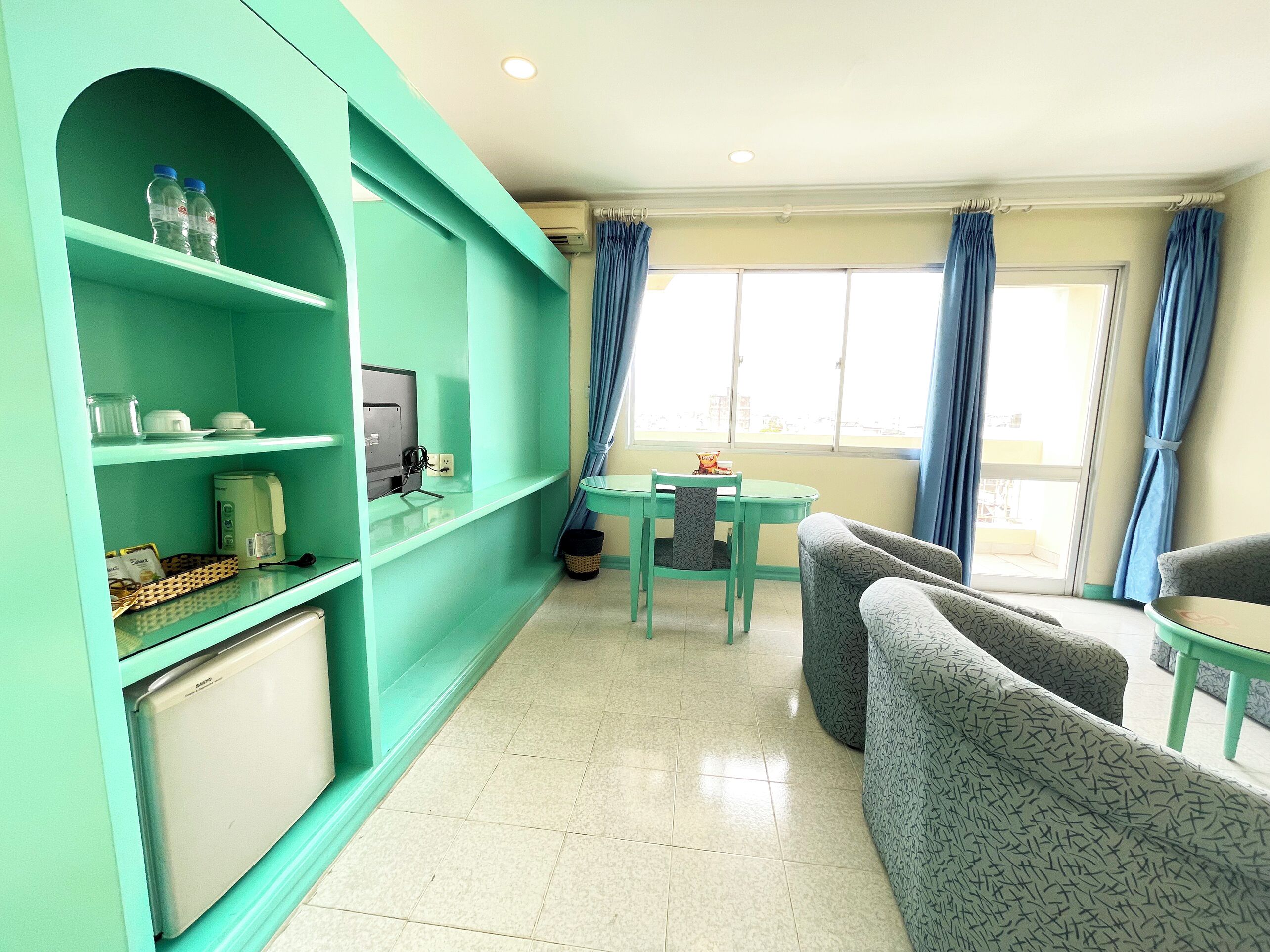 A teal-colored room with a television, a coffee maker, and a small table with chairs.