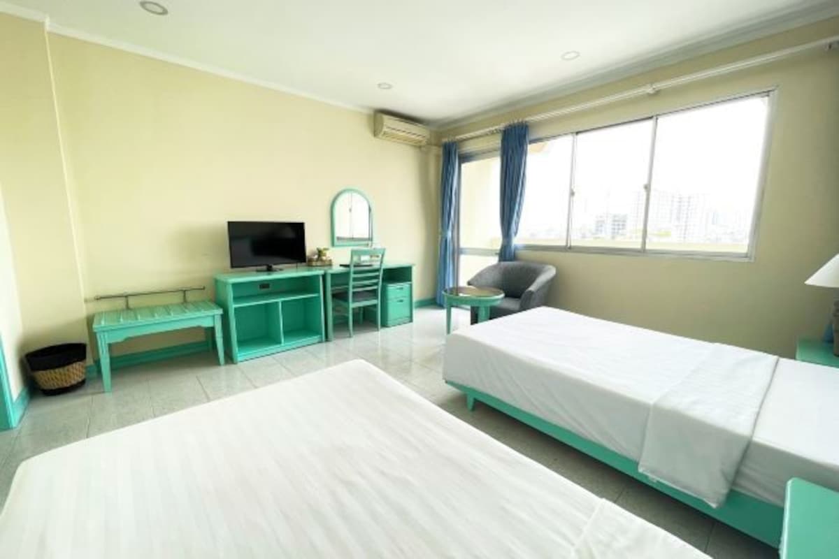 A hotel room with two beds, a desk with a TV, a chair, and a window with curtains.