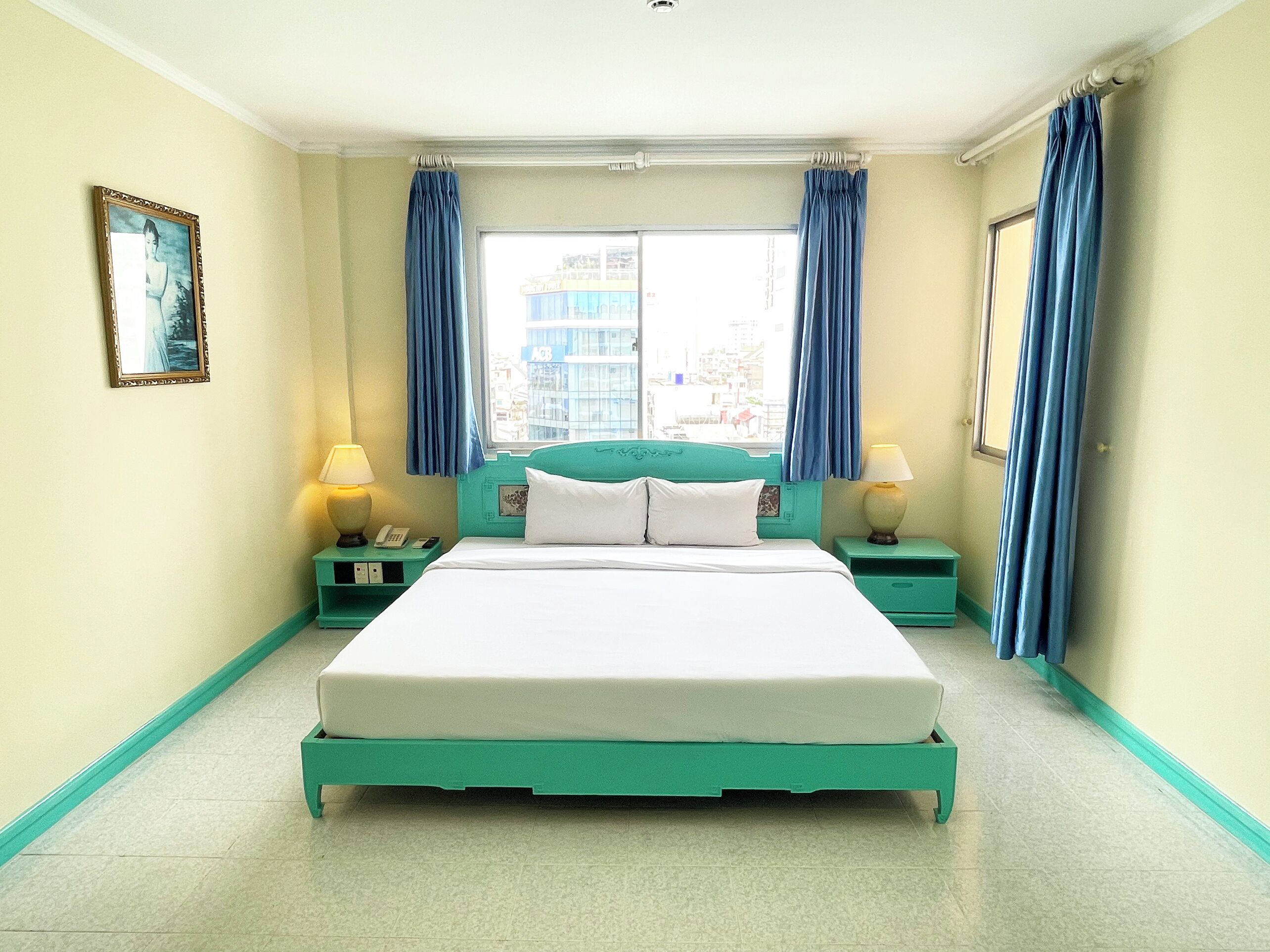 Une chambre d’hôtel avec un lit, deux tables de chevet, une fenêtre avec des rideaux et un tableau encadré au mur.