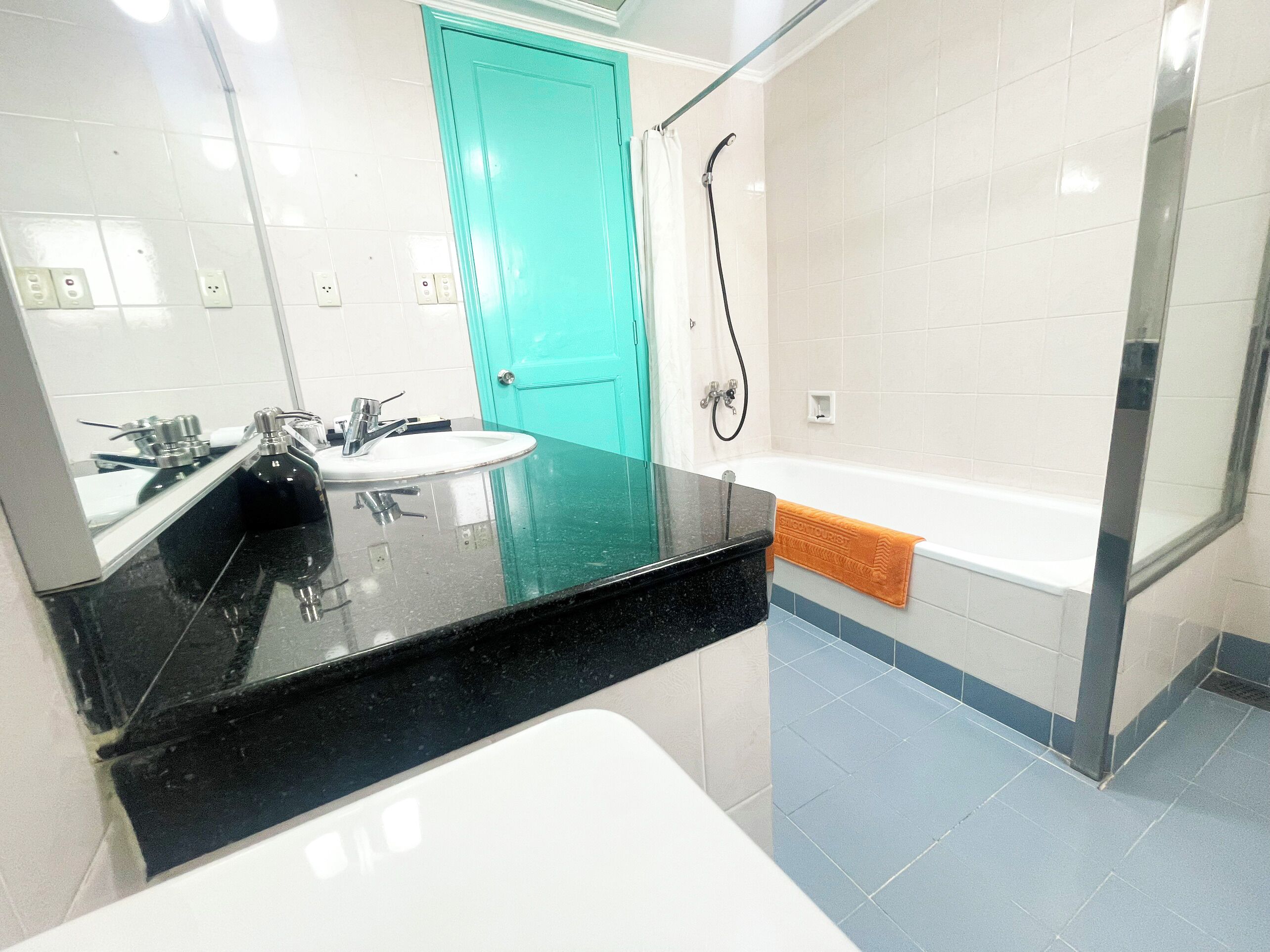 Un baño moderno con encimera negra, lavamanos blanco y ducha con puerta de cristal.