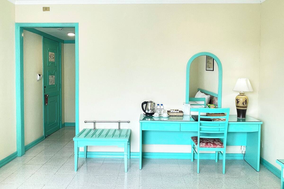 Una habitación con un escritorio color turquesa, un banco, un espejo y una lámpara.