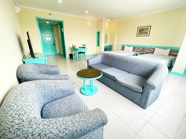 Habitación de hotel con sofá, dos sillones, una mesita redonda, cama, escritorio y silla.