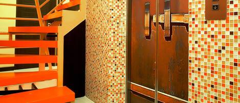 A modern elevator with a mosaic tile wall, a metal staircase, and a control panel.