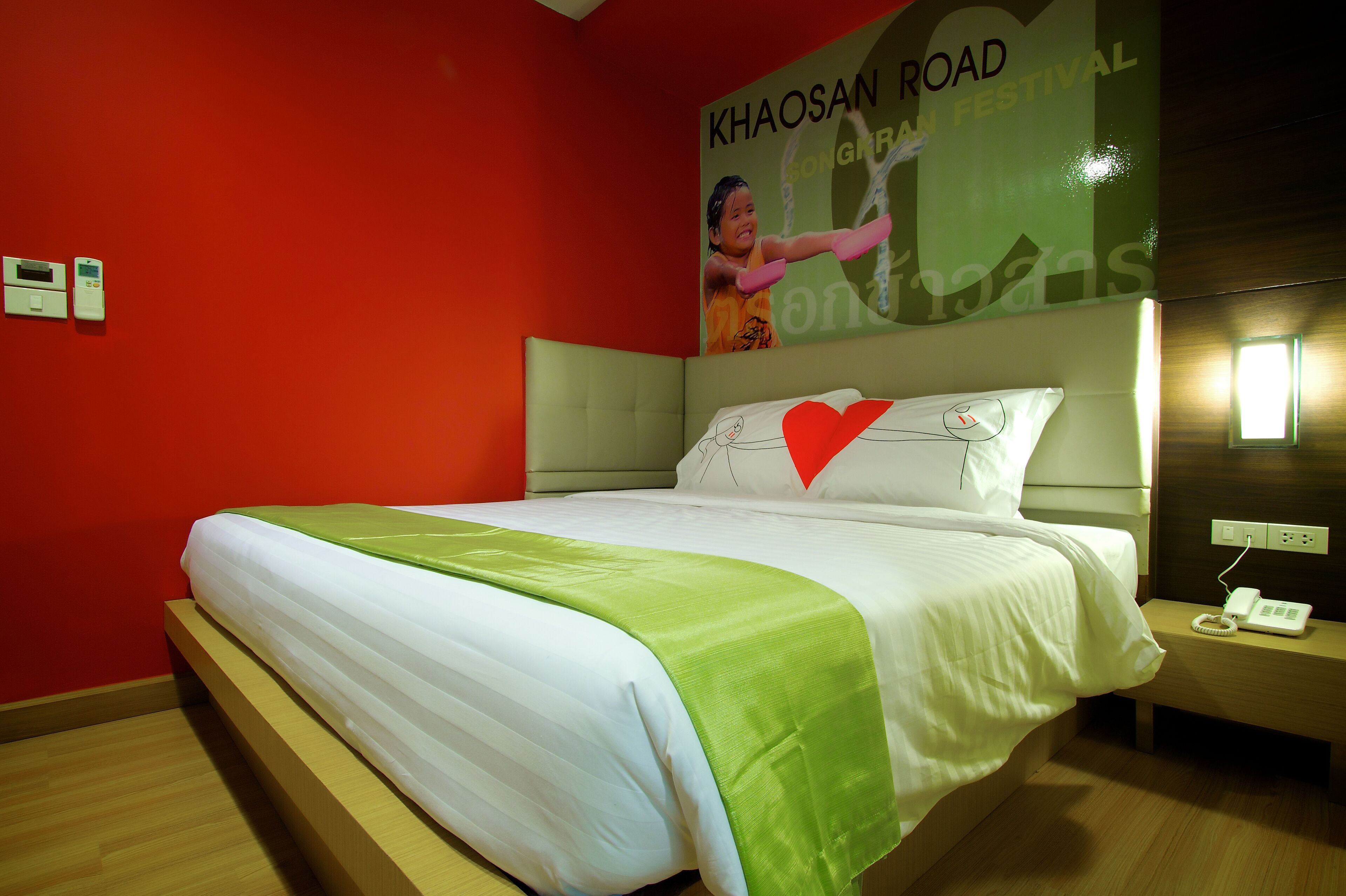 Habitació d'hotel amb un llit, un edredó verd i blanc, una paret vermella i un cartell a la paret.