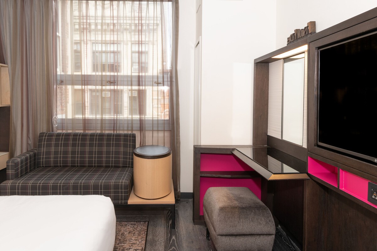 A hotel room with a bed, a sofa, a small table, a TV, and a window with curtains.