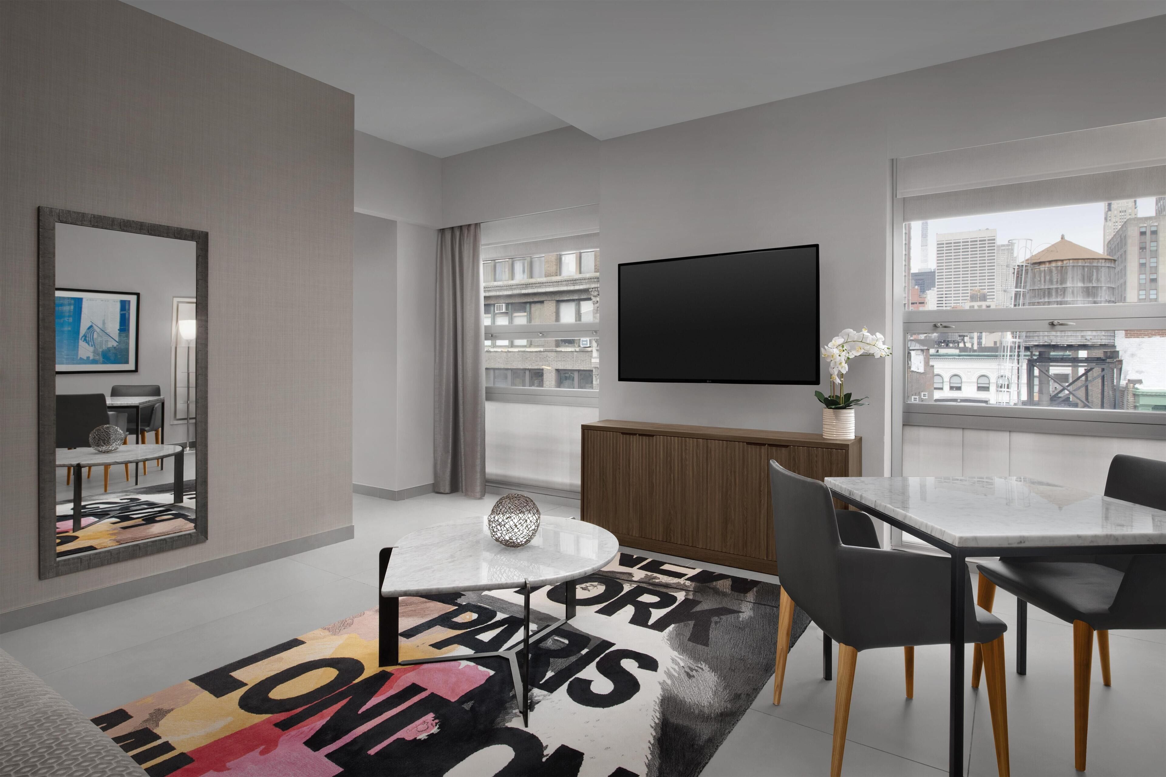 Una habitación de hotel moderna con zona de comedor, televisor de pantalla plana y vistas a la ciudad.