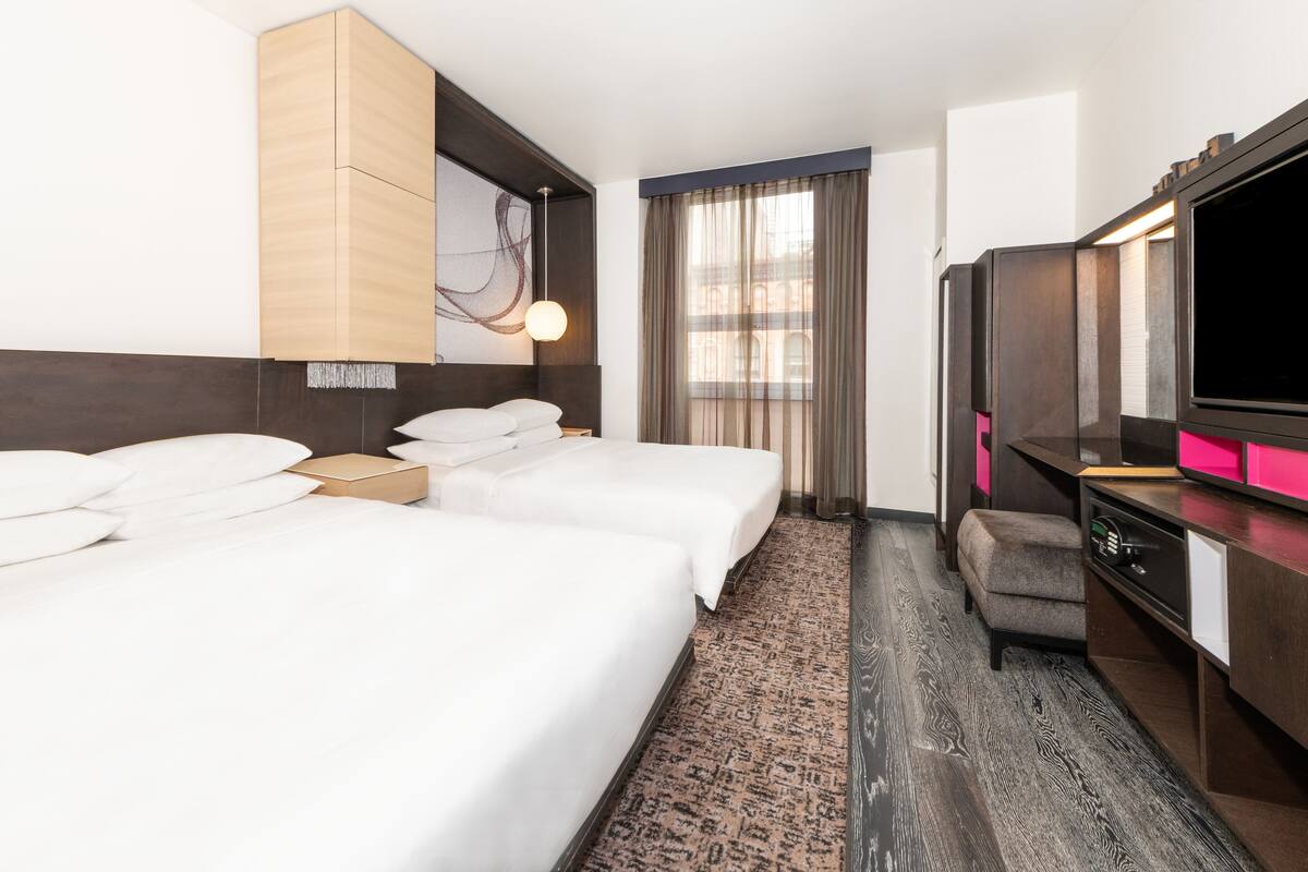 A hotel room with two beds, a TV, a desk, and a window with curtains.