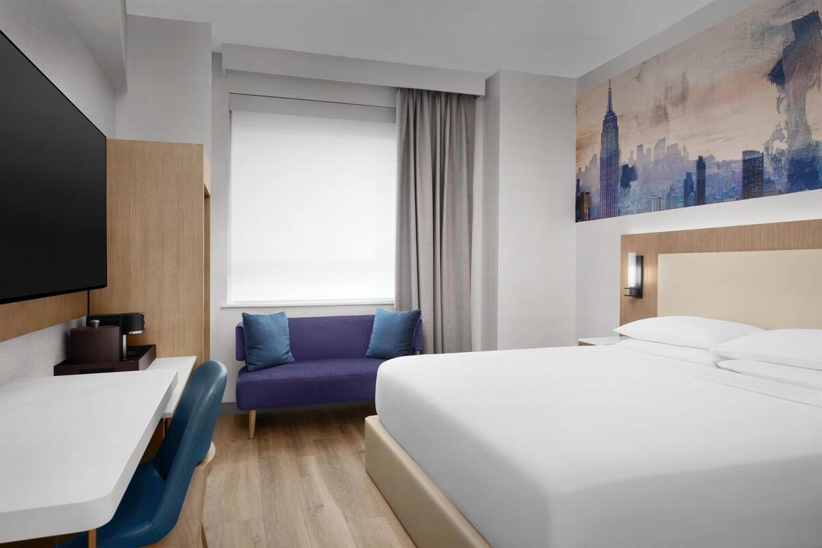A hotel room with a bed, a sofa, a desk, and a TV.