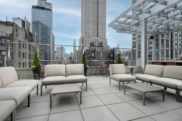 Terraza en la azotea con mobiliario moderno, zona de bar y vistas al horizonte de la ciudad.