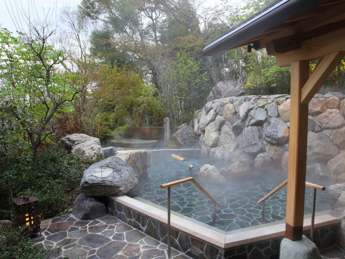 A hot spring area with stone steps, wooden railings, and a stone wall backdrop.