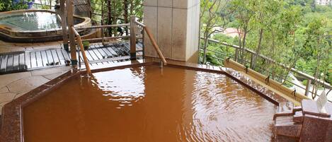 A hot spring bath area with wooden steps leading into the water, surrounded by a wooden railing.