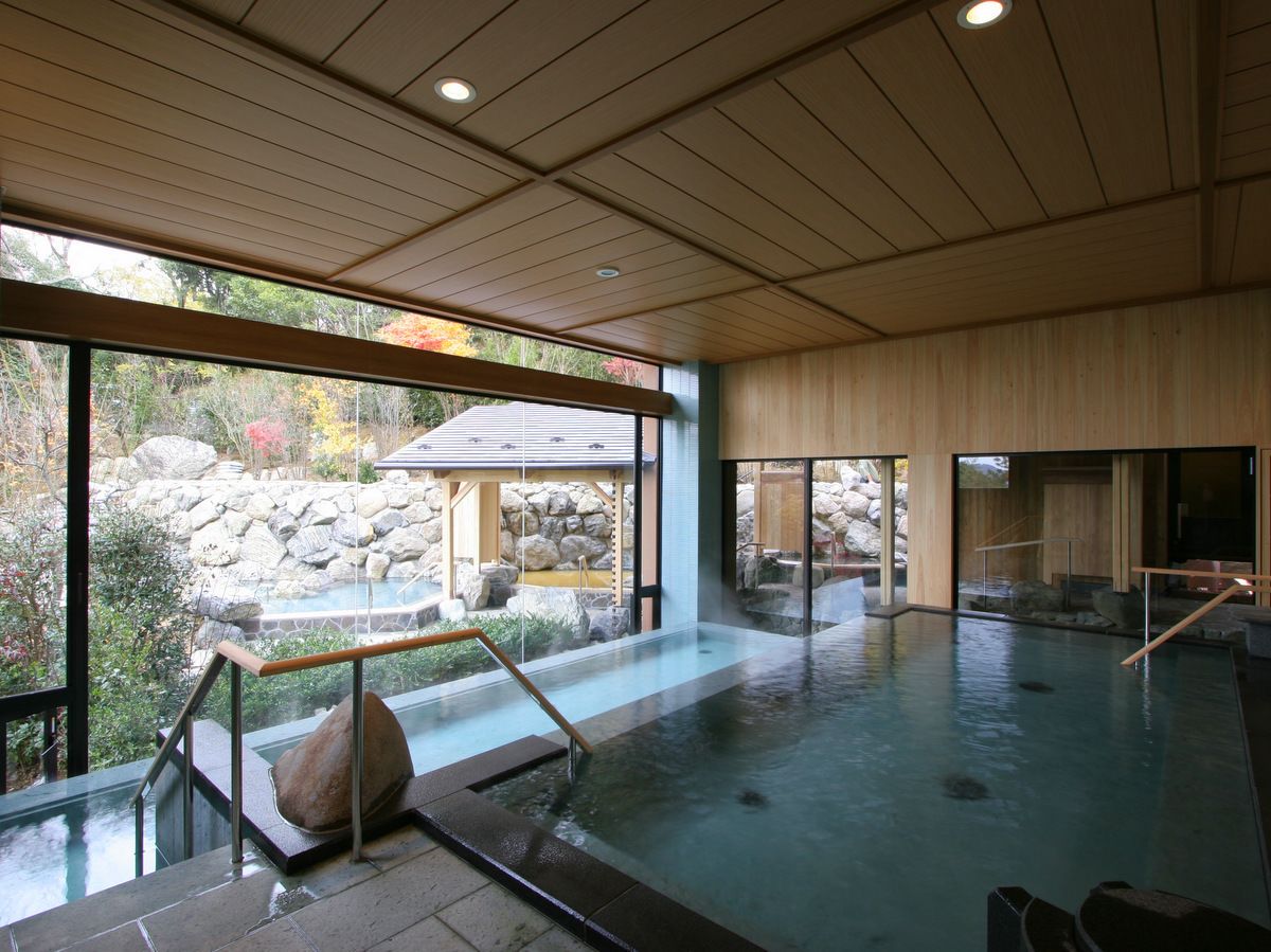 A large indoor hot spring bath with a view of a stone garden and a wooden structure outside.