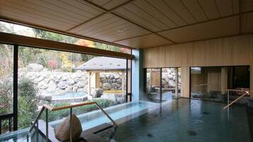 A large indoor hot spring bath with a view of a stone garden and a wooden structure outside.