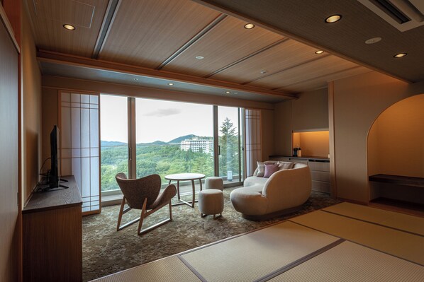 Una sala de estar moderna con un ventanal grande, un sofá, una silla, una mesita y un televisor sobre un mueble de madera.
