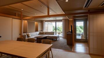 Una habitación amplia con una gran mesa de madera, un sofá y un televisor. Hay una puerta corrediza que da a un área exterior.