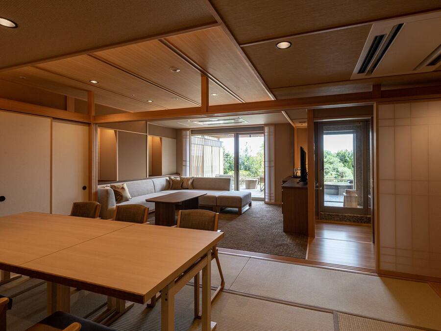 Una habitación amplia con una gran mesa de madera, un sofá y un televisor. Hay una puerta corrediza que da a un área exterior.