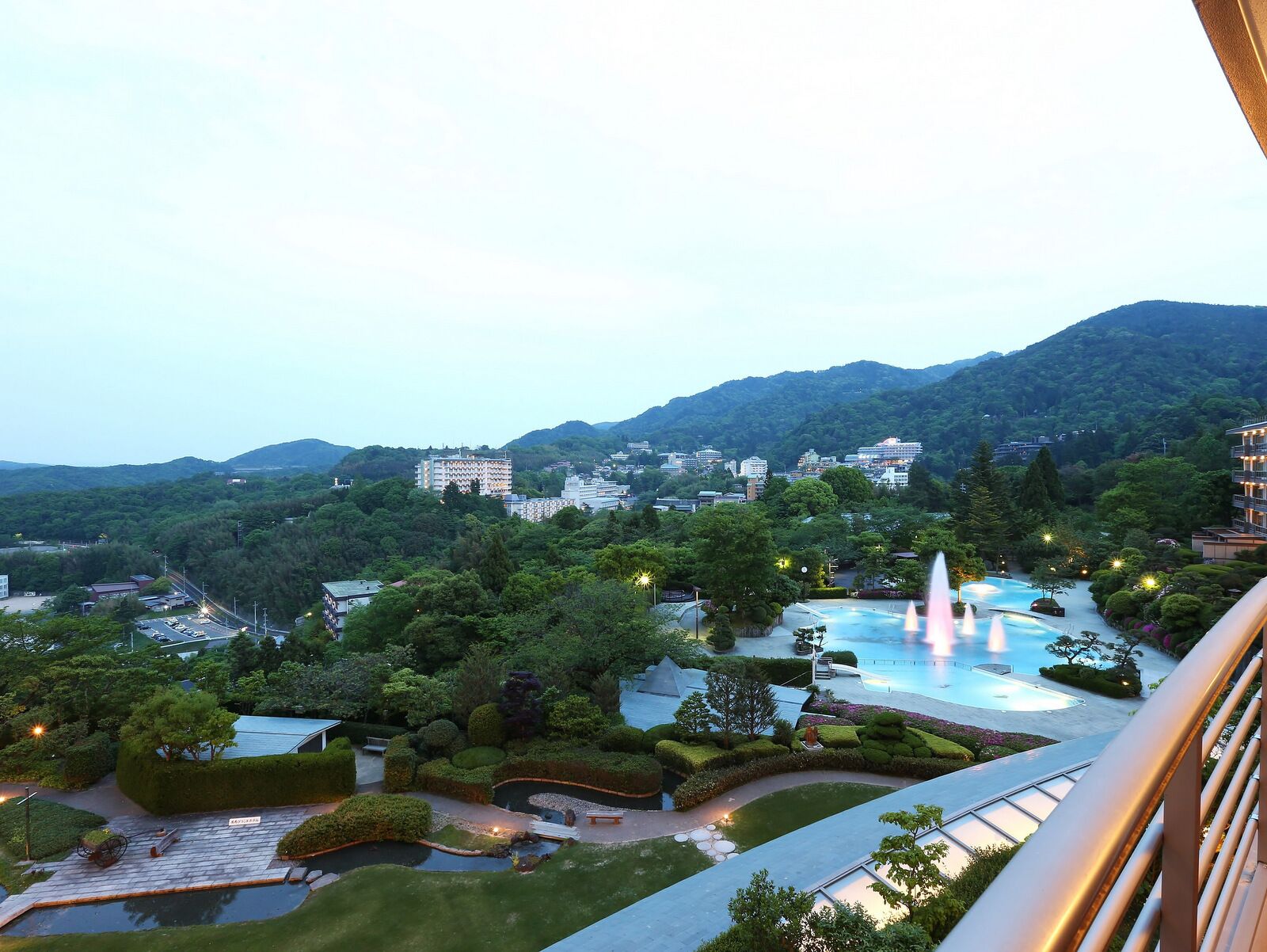 Un resort con una gran piscina, jardines cuidados y vistas de edificios y colinas circundantes.