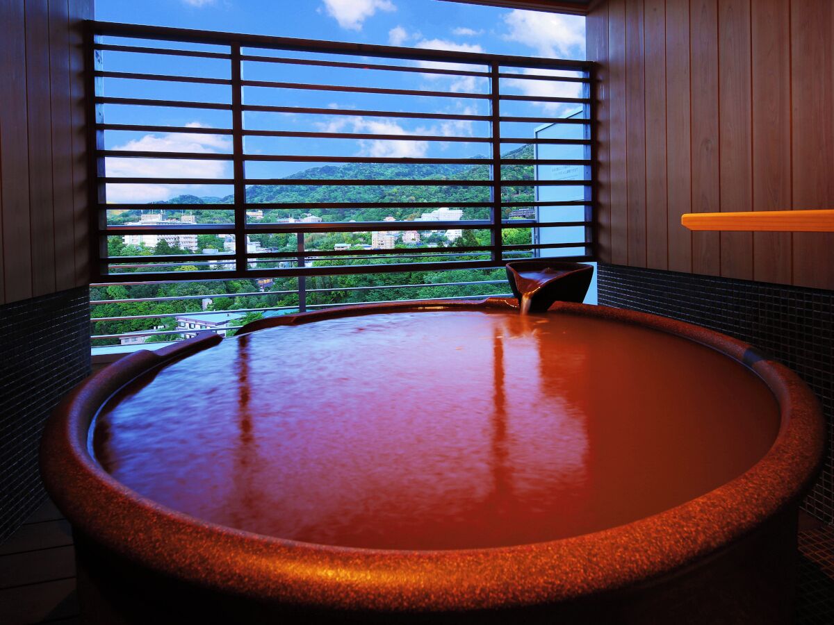 Un jacuzzi con vista a un paisaje urbano a través de una ventana con persianas horizontales.