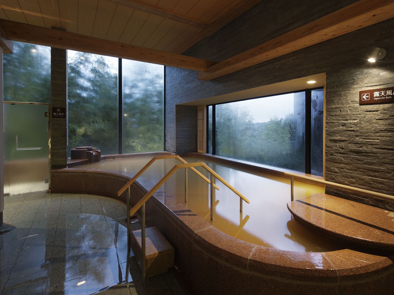 A modern bathroom with a stone sink, wooden railings, and large windows.