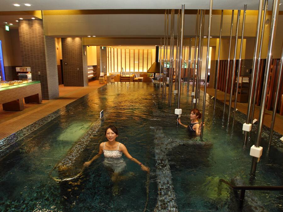 Uma área de piscina com uma piscina comprida e estreita, um balcão de recepção e áreas de estar.