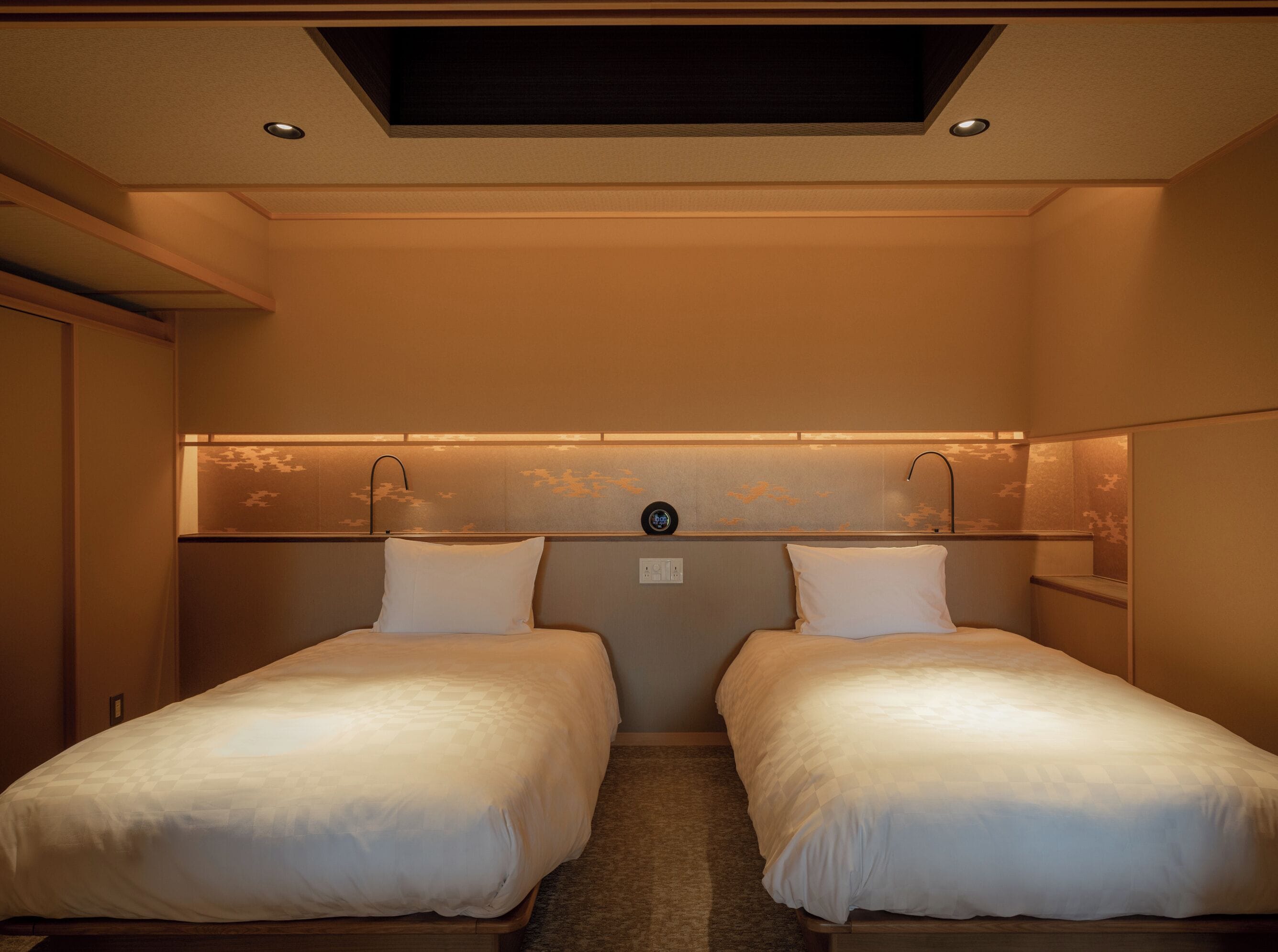 A hotel room with two single beds, a skylight, and a wall-mounted clock.