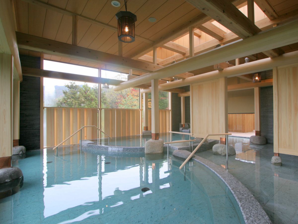 A spa pool with wooden beams, stone steps, and a view of trees outside.