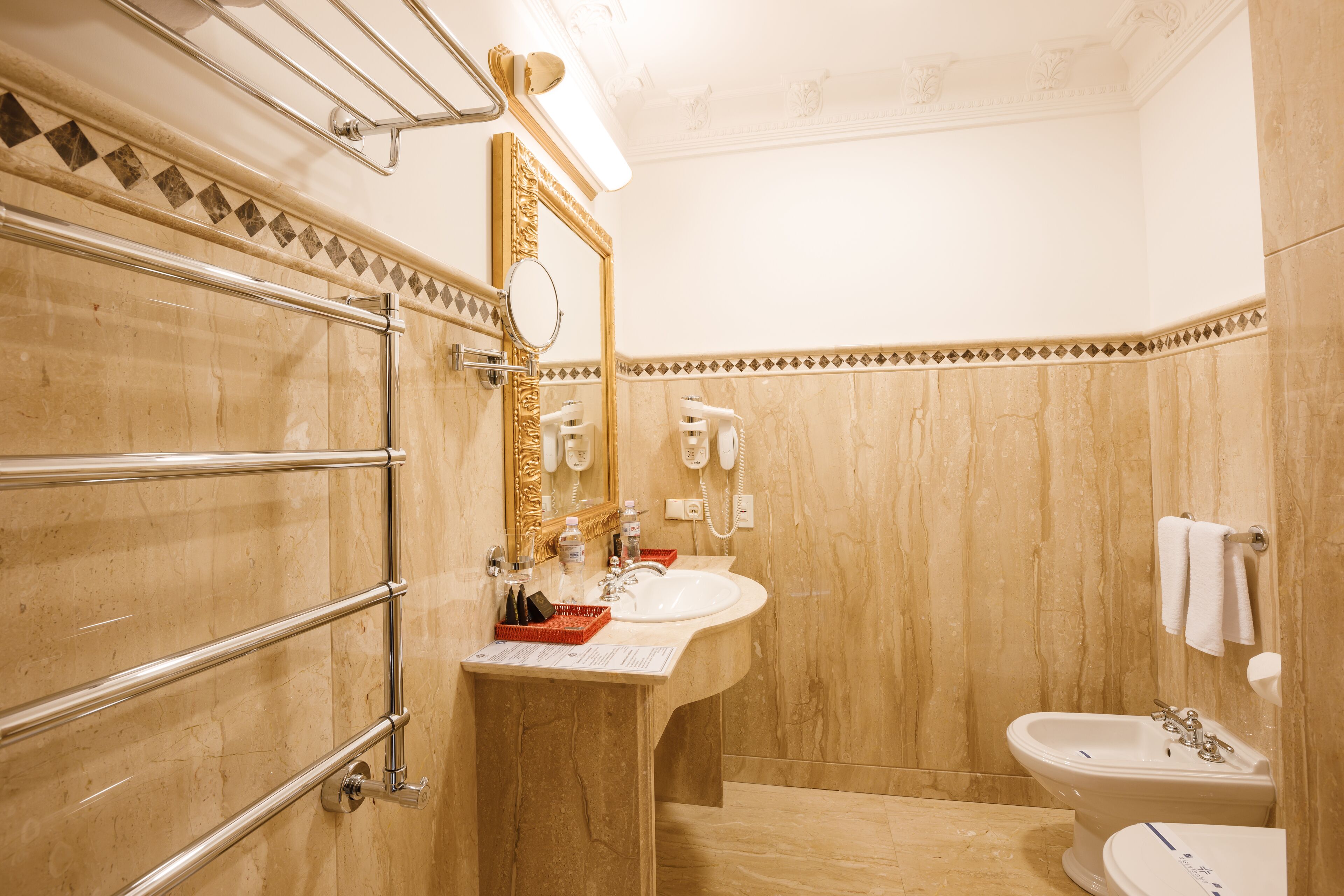 A bathroom with a marble sink, a vanity with a mirror, a towel rack, and a bidet.