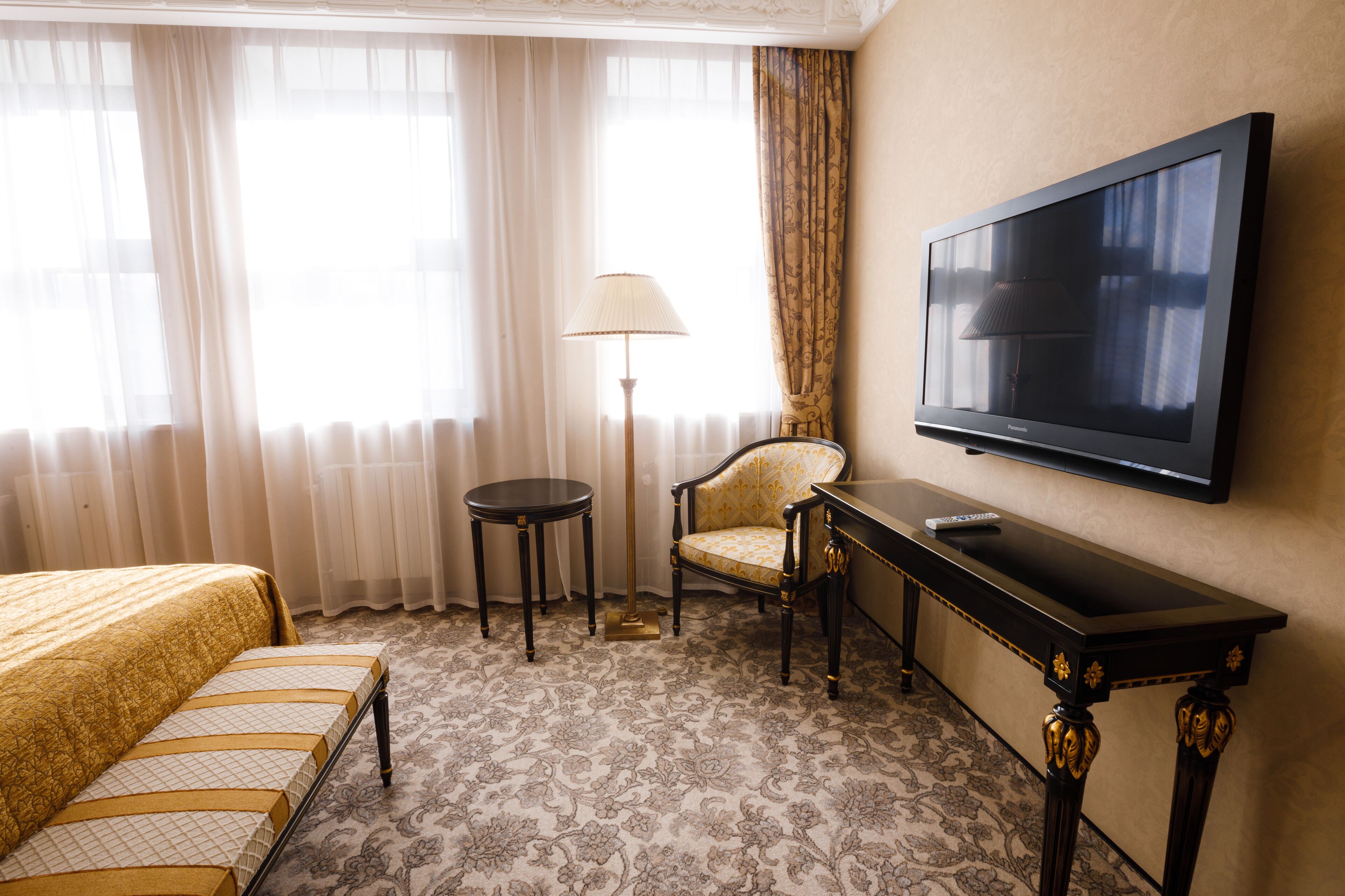 A hotel room with a bed, a chair, a small table, a lamp, and a TV on the wall.