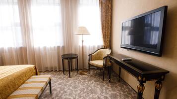 A hotel room with a bed, a chair, a small table, a lamp, and a TV on the wall.