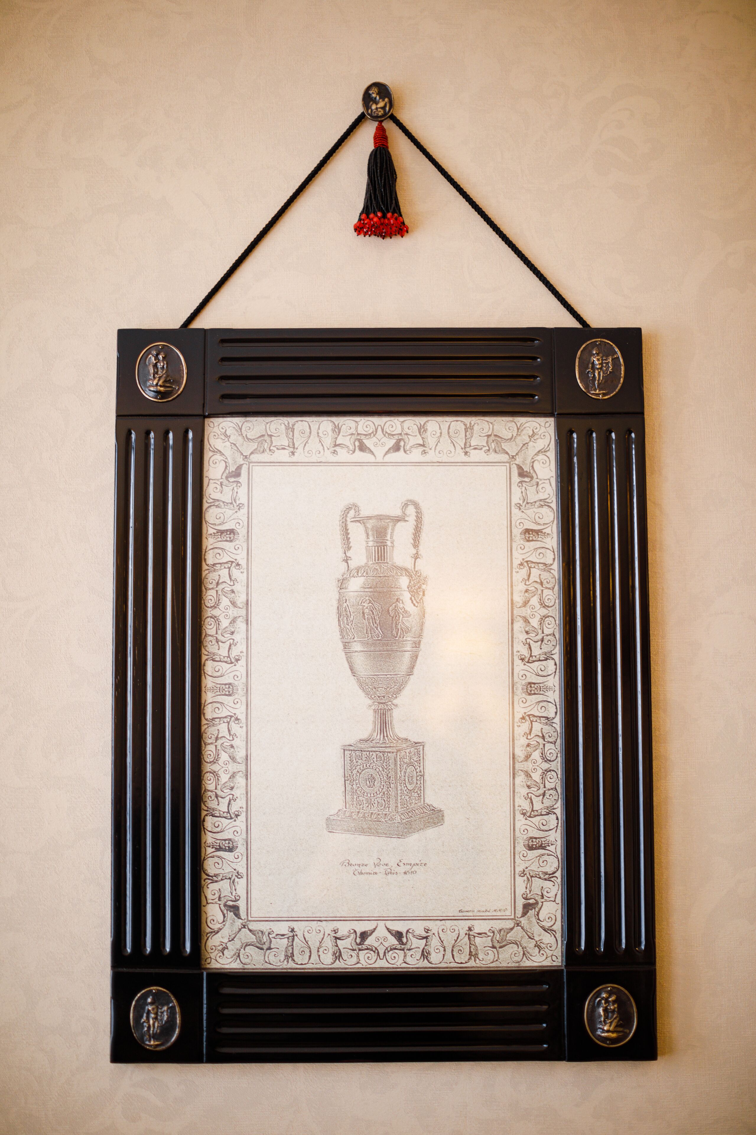 A framed artwork of a trophy with a tassel hanging above it.