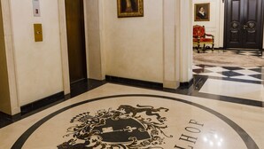 Um saguão com um emblema circular, um elevador e um candelabro.