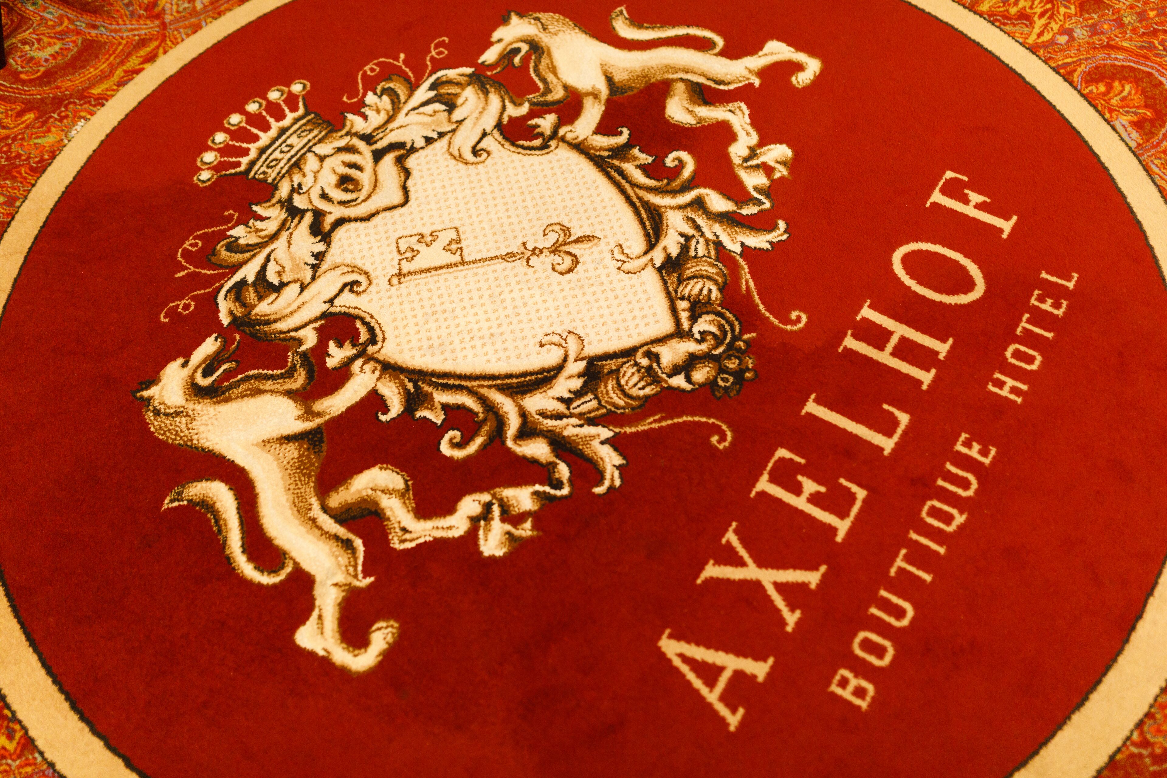 Een cirkelvormig embleem met een wapenschild en de tekst 'AXELHOF BOUTIQUE HOTEL'.