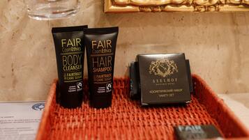 A bathroom vanity with a gold-framed mirror, a red woven tray holding two body cleansers and a hair shampoo, and a small black box labeled "AXELHOF".