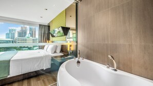A modern hotel room with a large bathtub, a bed, and a city view through a large window. - The Mandison Bangkok (formerly Golden Tulip Mandison Suites) (Bangkok)