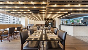 A modern restaurant with long tables, black leather chairs, and a bar area with a view of the city. - The Mandison Bangkok (formerly Golden Tulip Mandison Suites) (Bangkok)