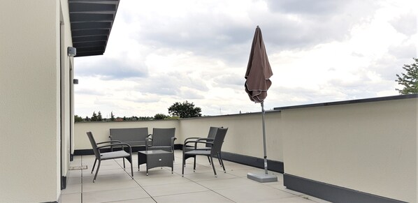An outdoor patio with a table and chairs, a covered umbrella, and a view of the sky.