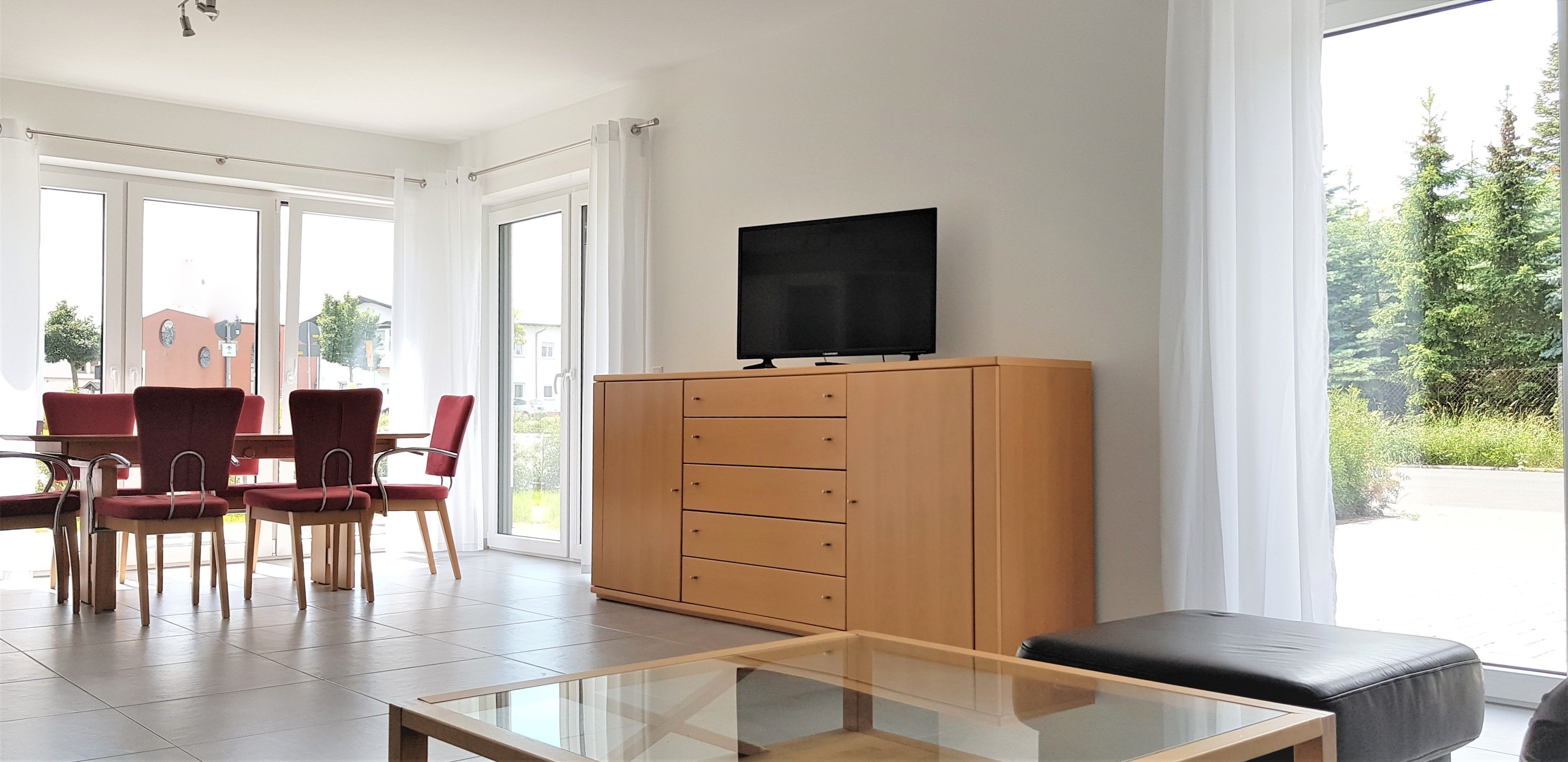 A modern living room with a glass coffee table, a wooden cabinet, and a flat-screen TV.