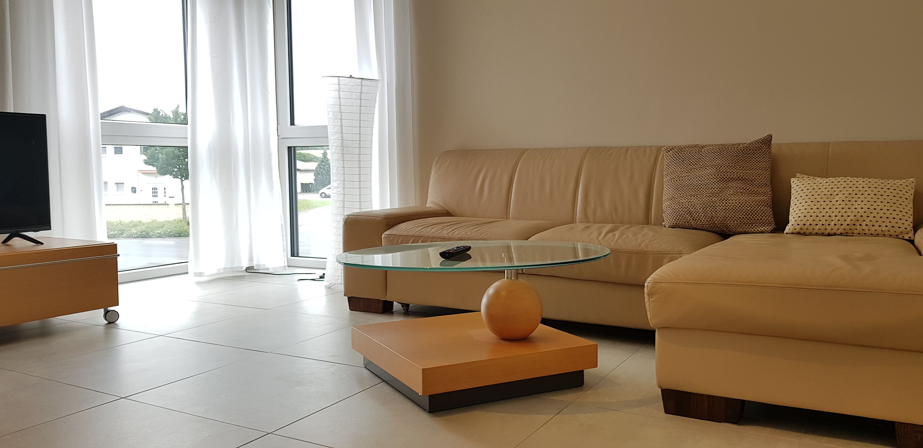 A modern living room with a beige sofa, a glass coffee table, and a wooden side table.