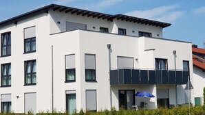 A modern two-story building with multiple windows, a balcony, and a door with a blue umbrella. - fewosi (Pohlheim)