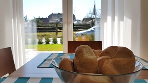 A glass bowl of bread on a table with a view of a house and a car through a window. - fewosi (Pohlheim)