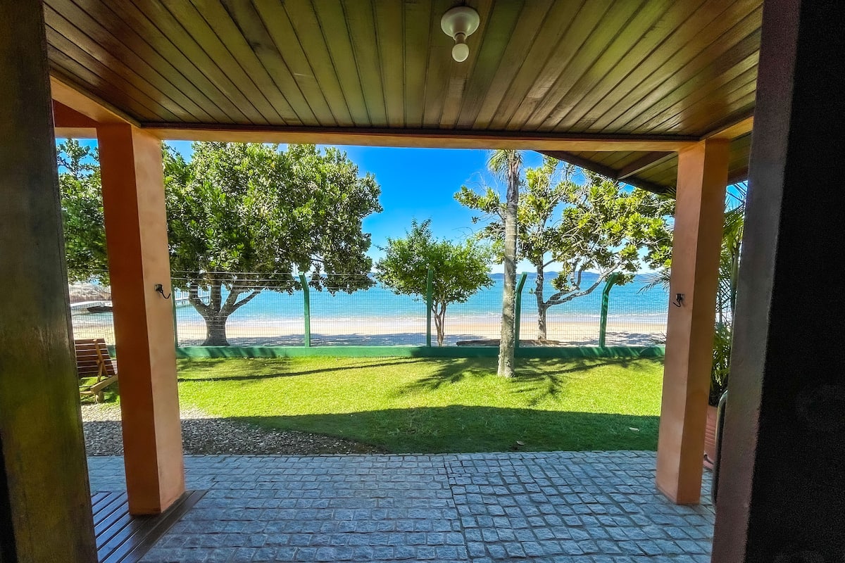 A covered patio with a view of a beach and trees.