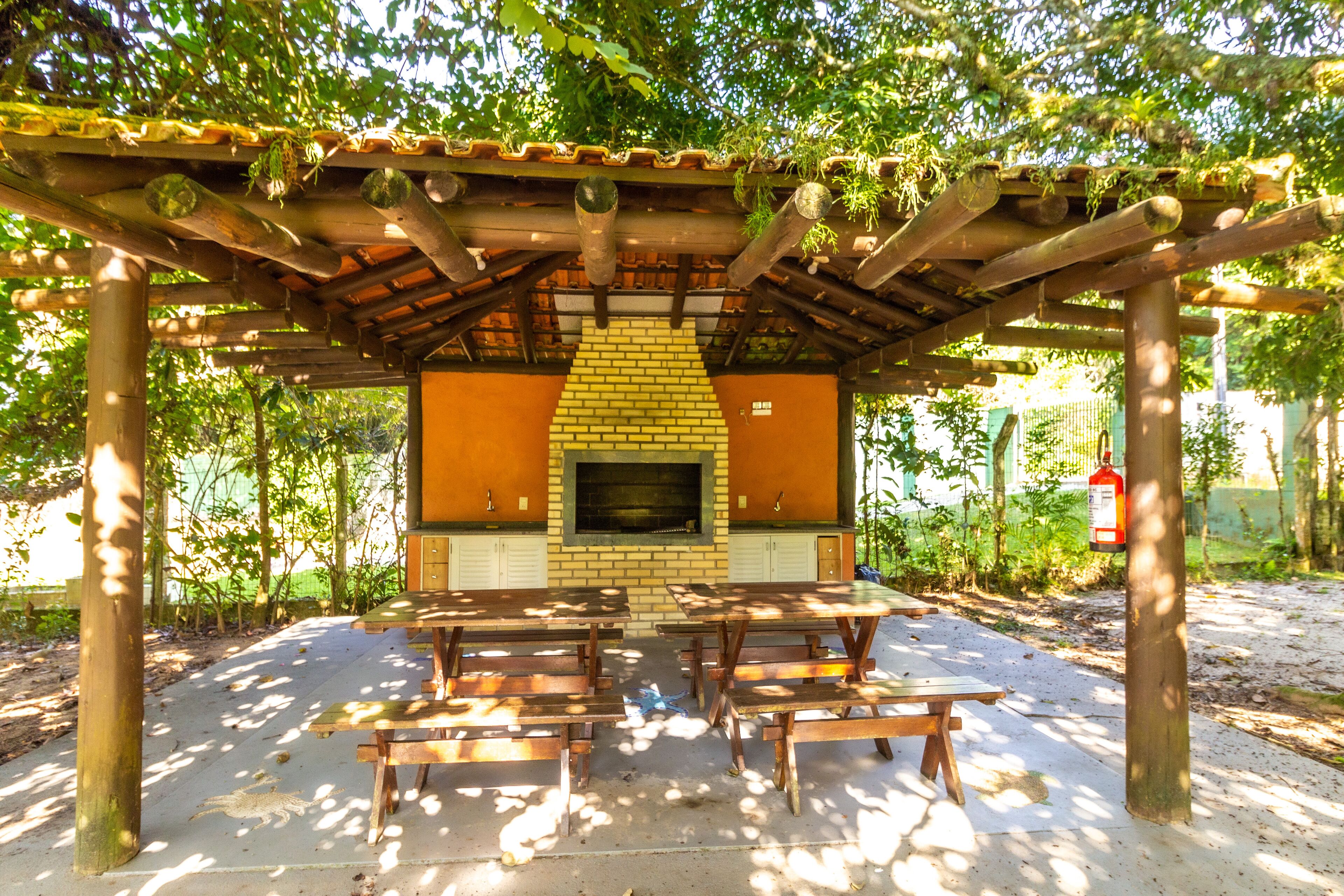 Une terrasse extérieure dotée d’une cheminée en briques, de tables en bois et d’une pergola couverte de plantes grimpantes.